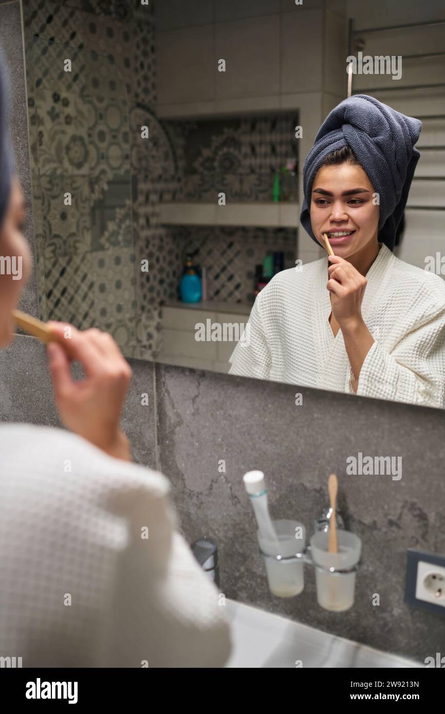 Young woman brushing teeth and looking in mirror at home Stock Photo