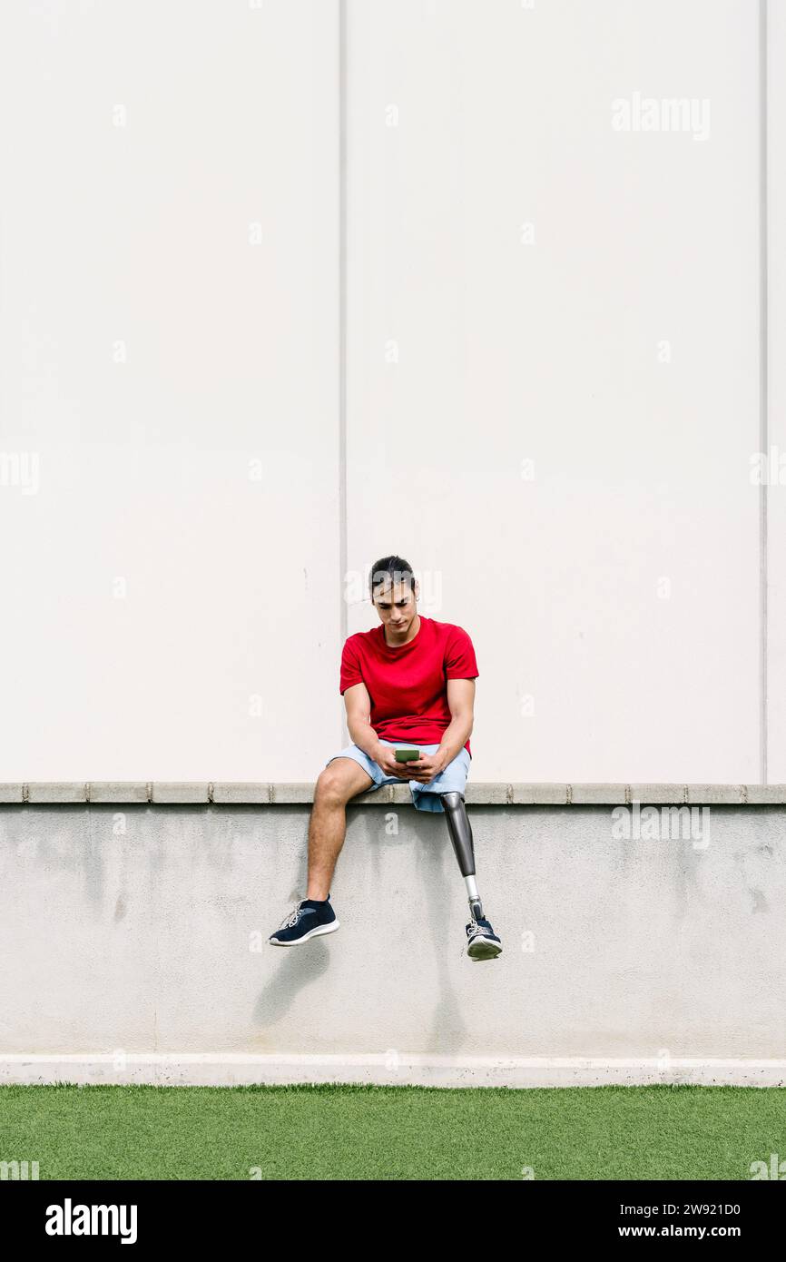 Man sitting with prosthetic leg and using smart phone on wall Stock Photo