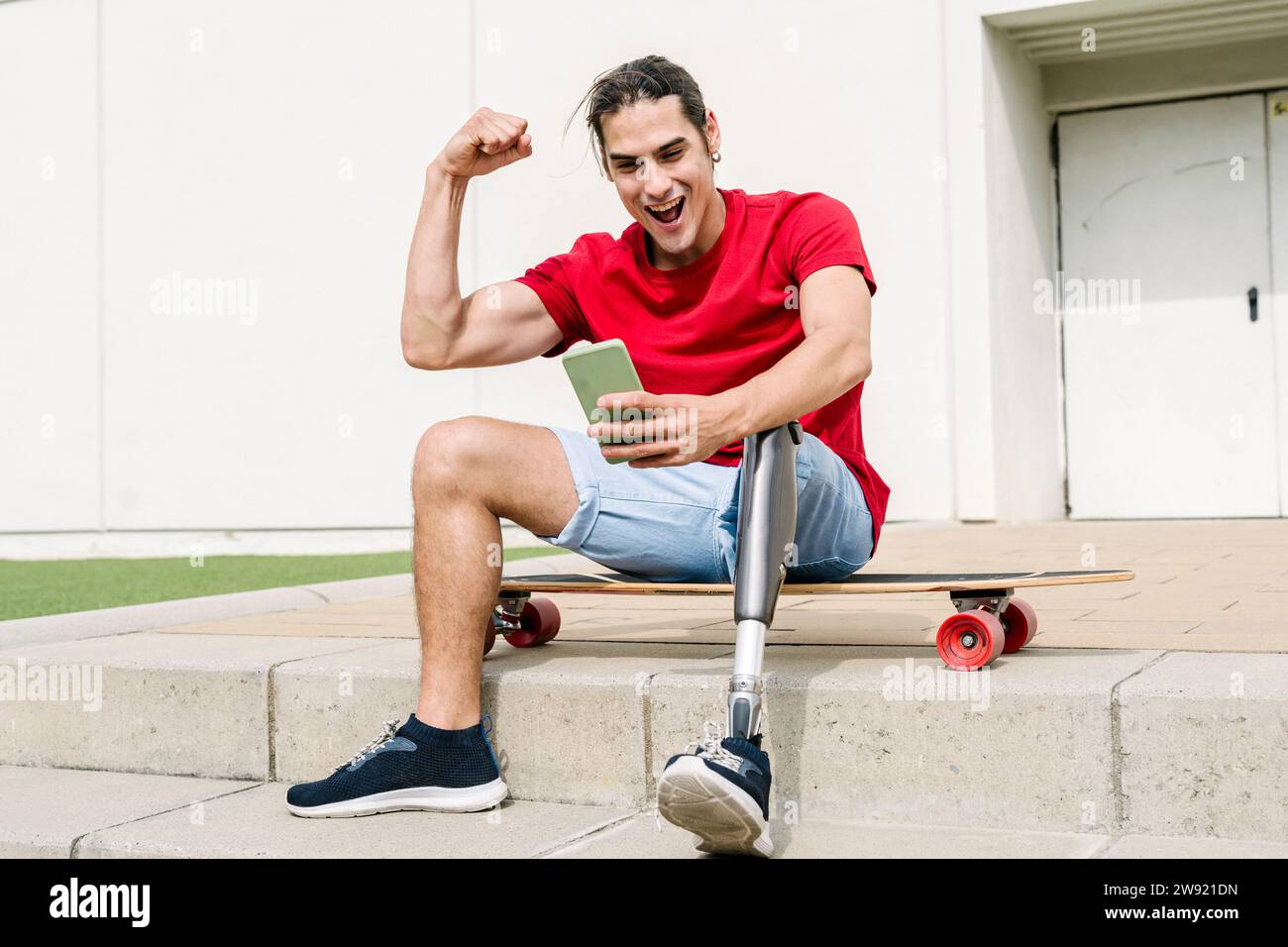 Cheerful man with disability flexing muscles and using mobile phone Stock Photo