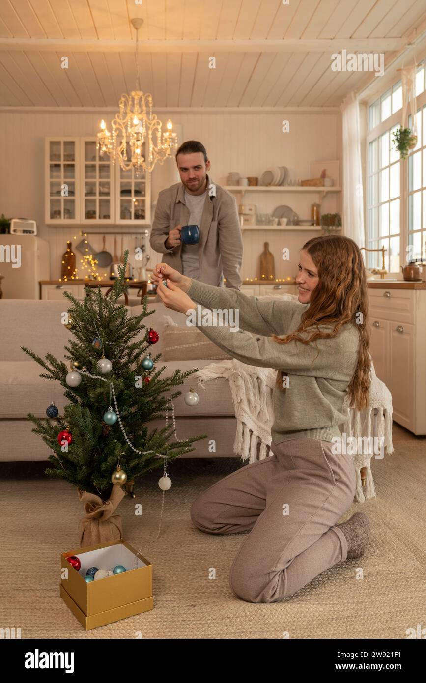 Smiling woman decorating Christmas tree with man standing at home Stock Photo
