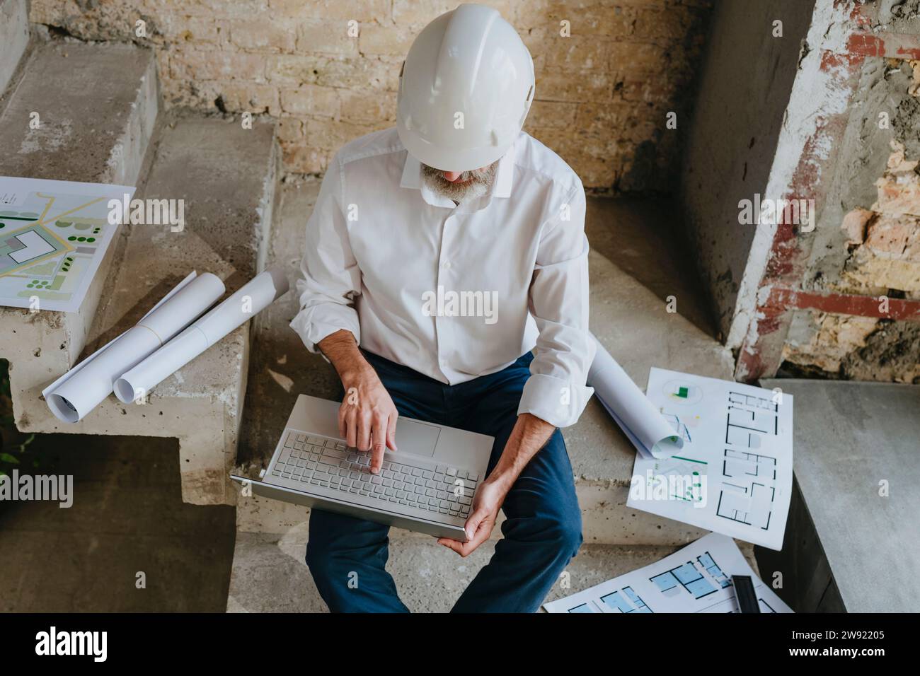 Architect using laptop with blueprints on staircase at site Stock Photo