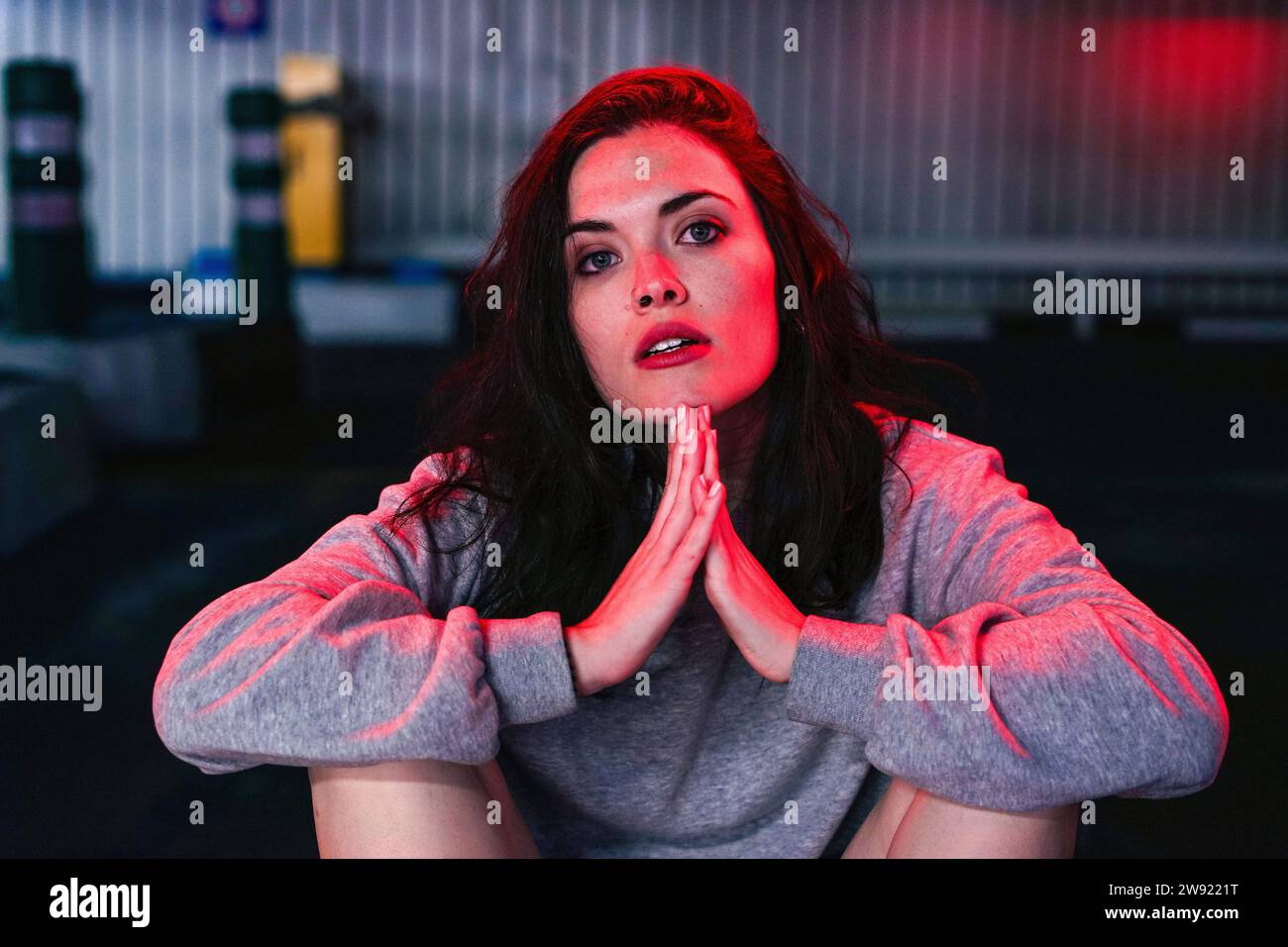 Woman sitting with hands clasped under red lighting Stock Photo