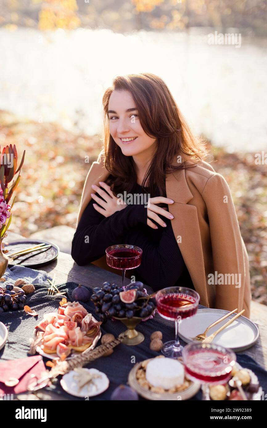 Smiling woman sitting at table for thanksgiving celebration in forest Stock Photo