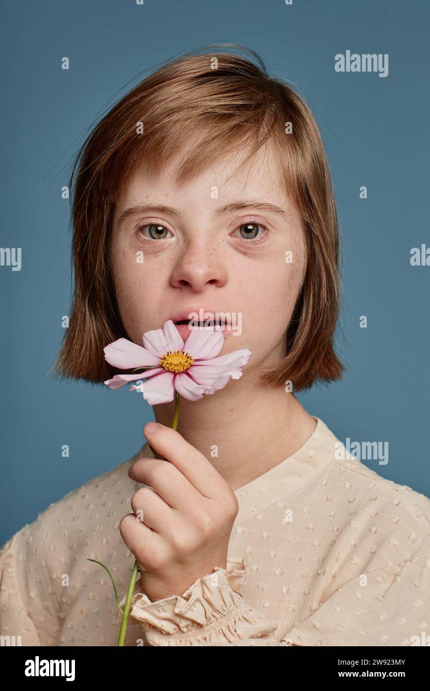 Girl with Down syndrome holding pink flower against blue background Stock Photo