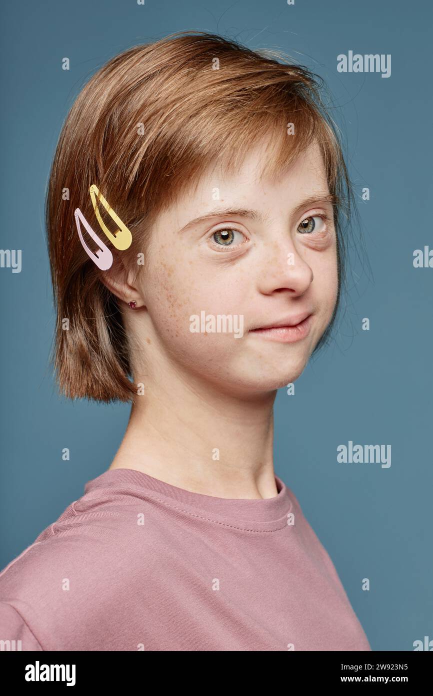 Girl with Down syndrome wearing hair clips by blue background Stock Photo