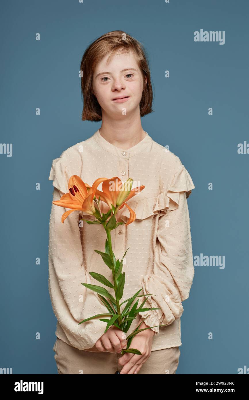 Teenage girl with Down syndrome holding orange orchid flower against blue background Stock Photo