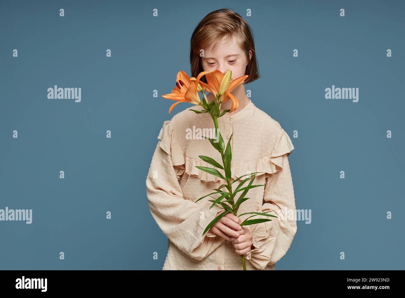 Teenage girl smelling orchid flowers standing against blue background Stock Photo