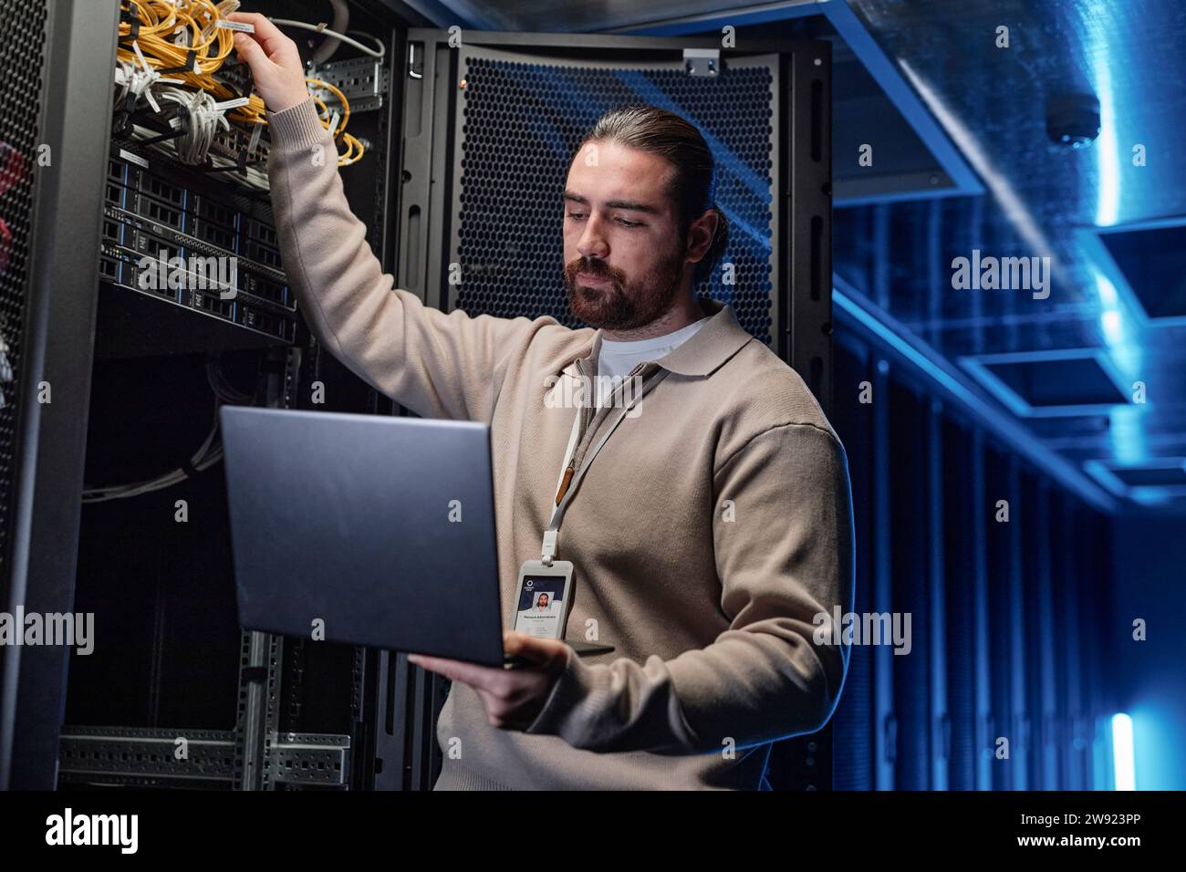 Young engineer touching cables and using laptop in server room Stock Photo