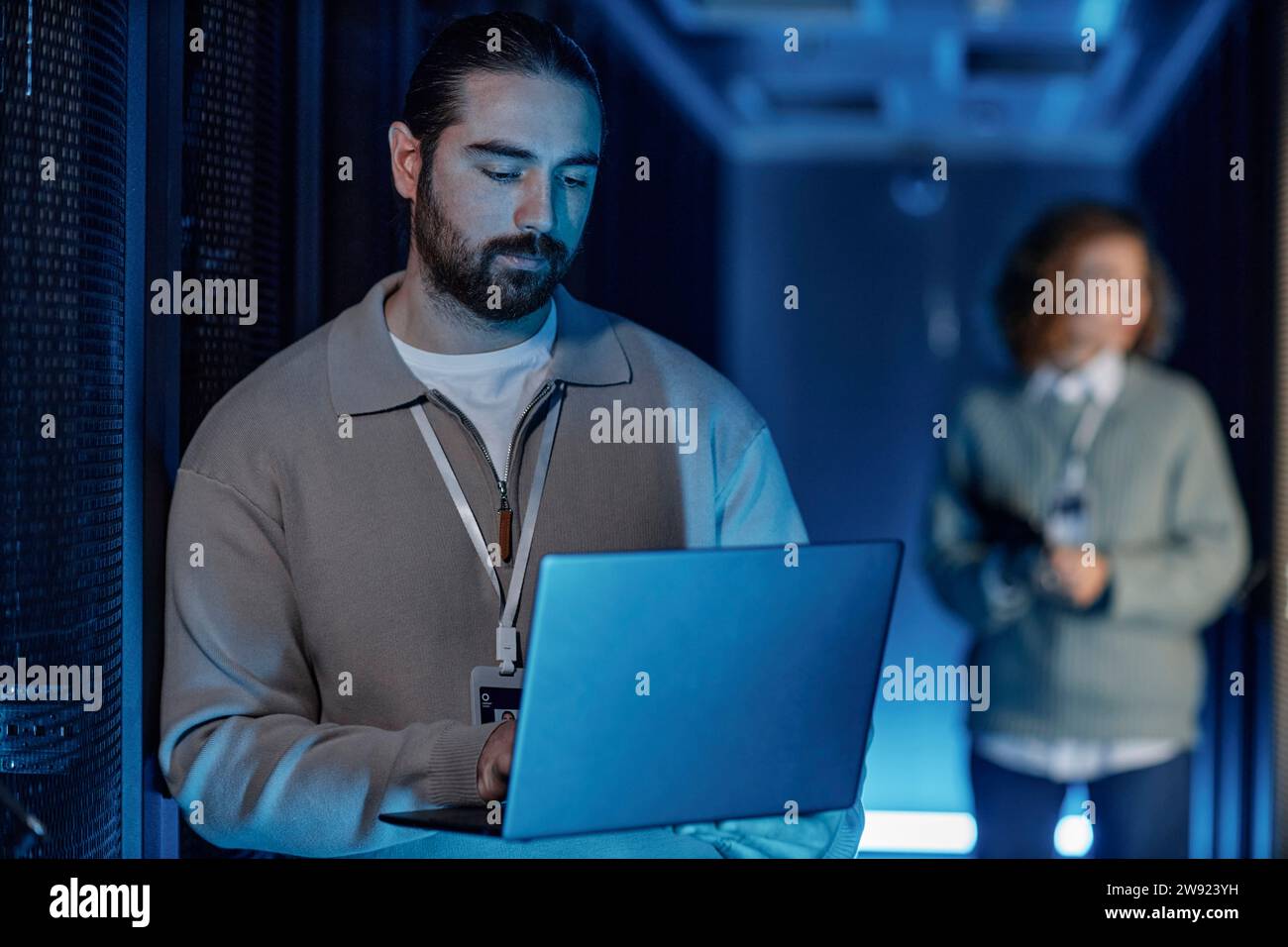 Young IT engineer using laptop with colleague standing in background Stock Photo