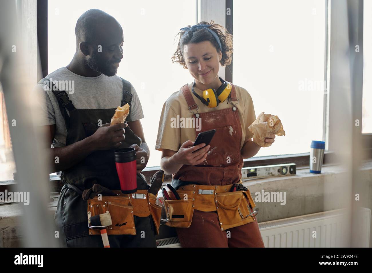 Smiling construction worker using smart phone and having lunch with coworker at site Stock Photo