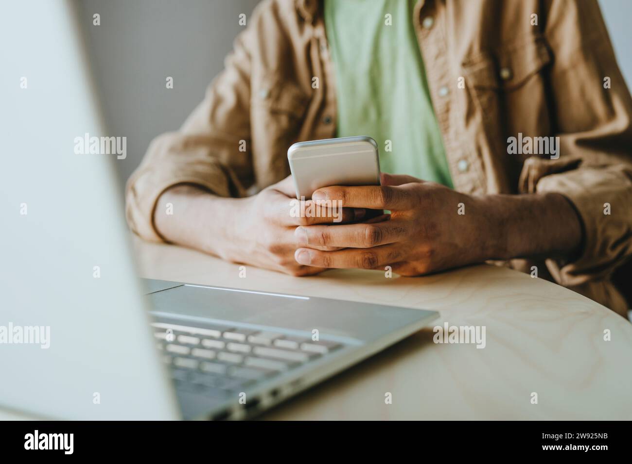 Man text messaging through smart phone by laptop on table at home Stock Photo