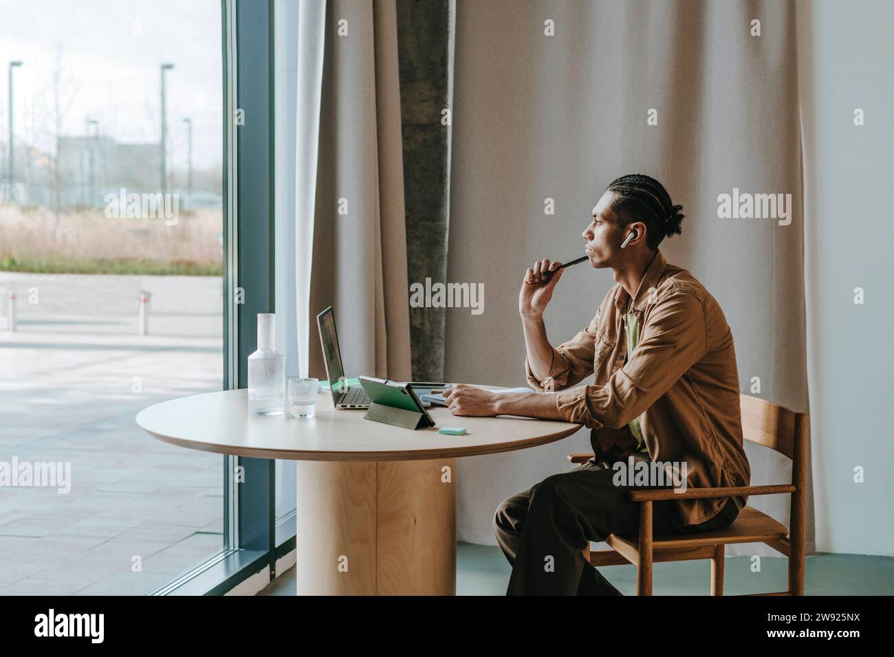 Thoughtful young man looking out through window sitting at table Stock Photo
