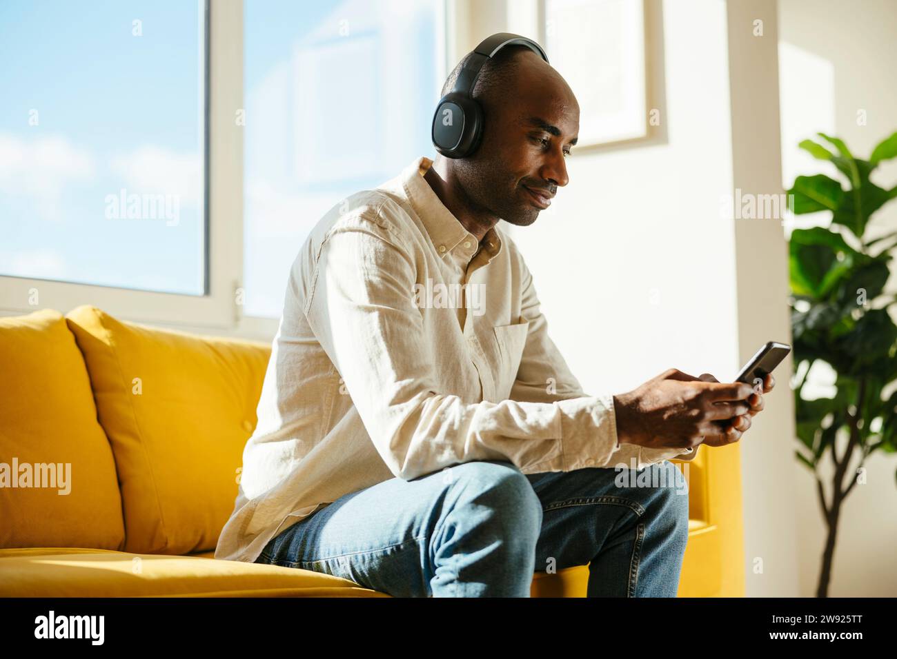 Businessman wearing wireless headphones using mobile phone sitting on sofa at home office Stock Photo