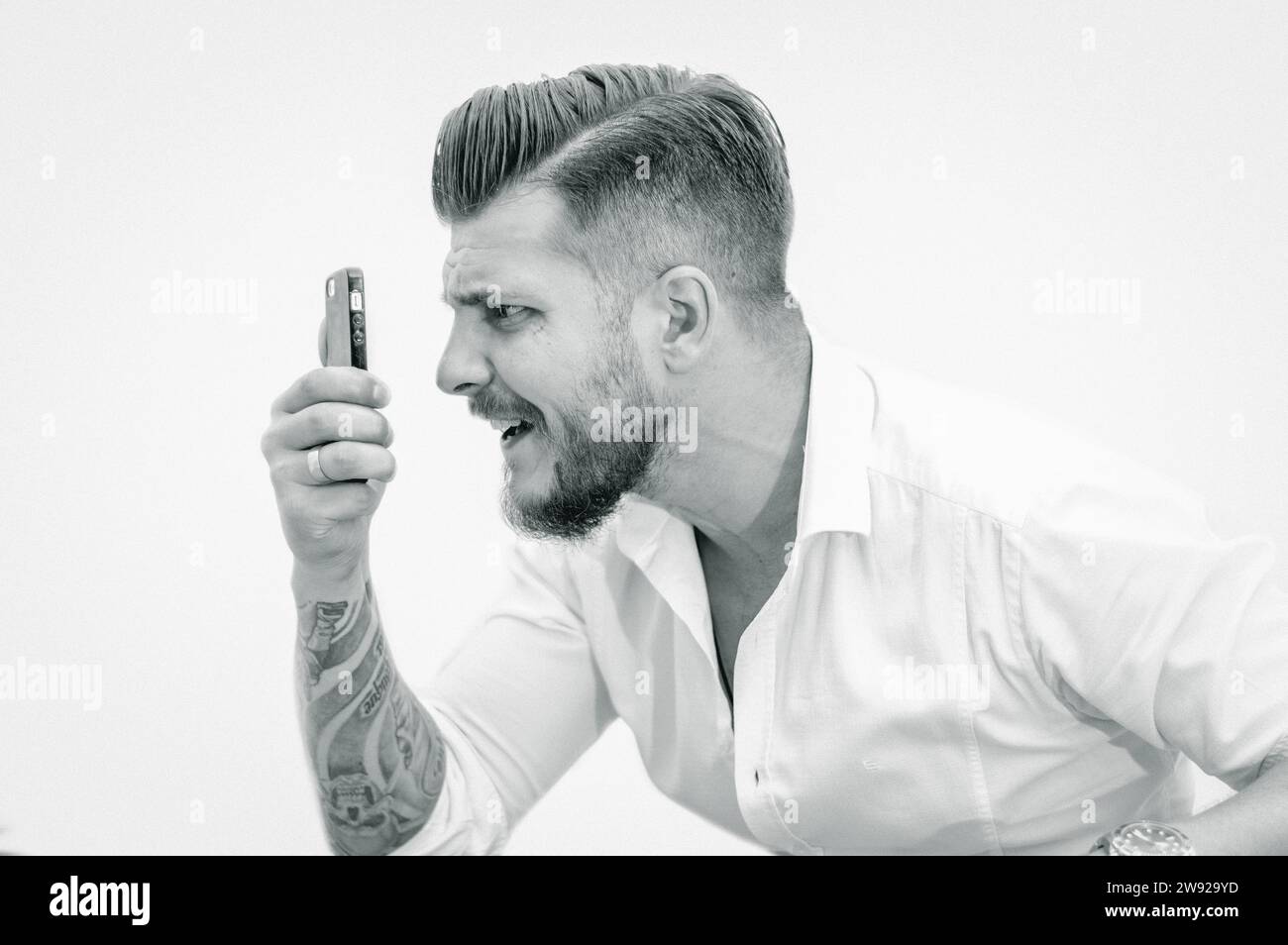 Man in a shirt looks at the smartphone screen in surprise. Concept of unsuccessful betting on games, fans, hippodrome. Mixed media Stock Photo