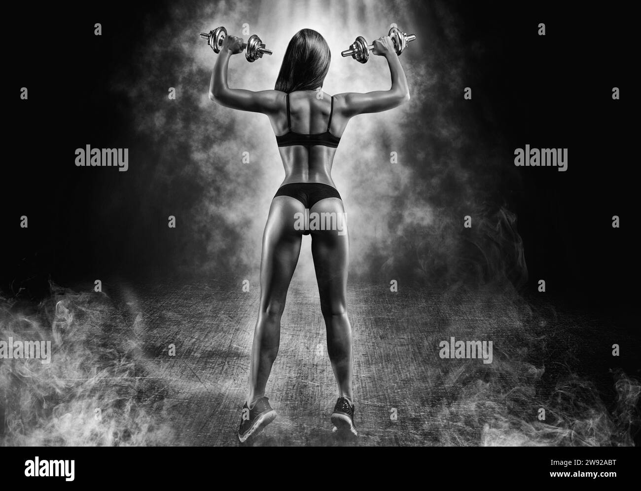 Tall adult woman with beautiful hair posing with dumbbells in her hand. Fitness and bodybuilding concept. Back view. Mixed media Stock Photo