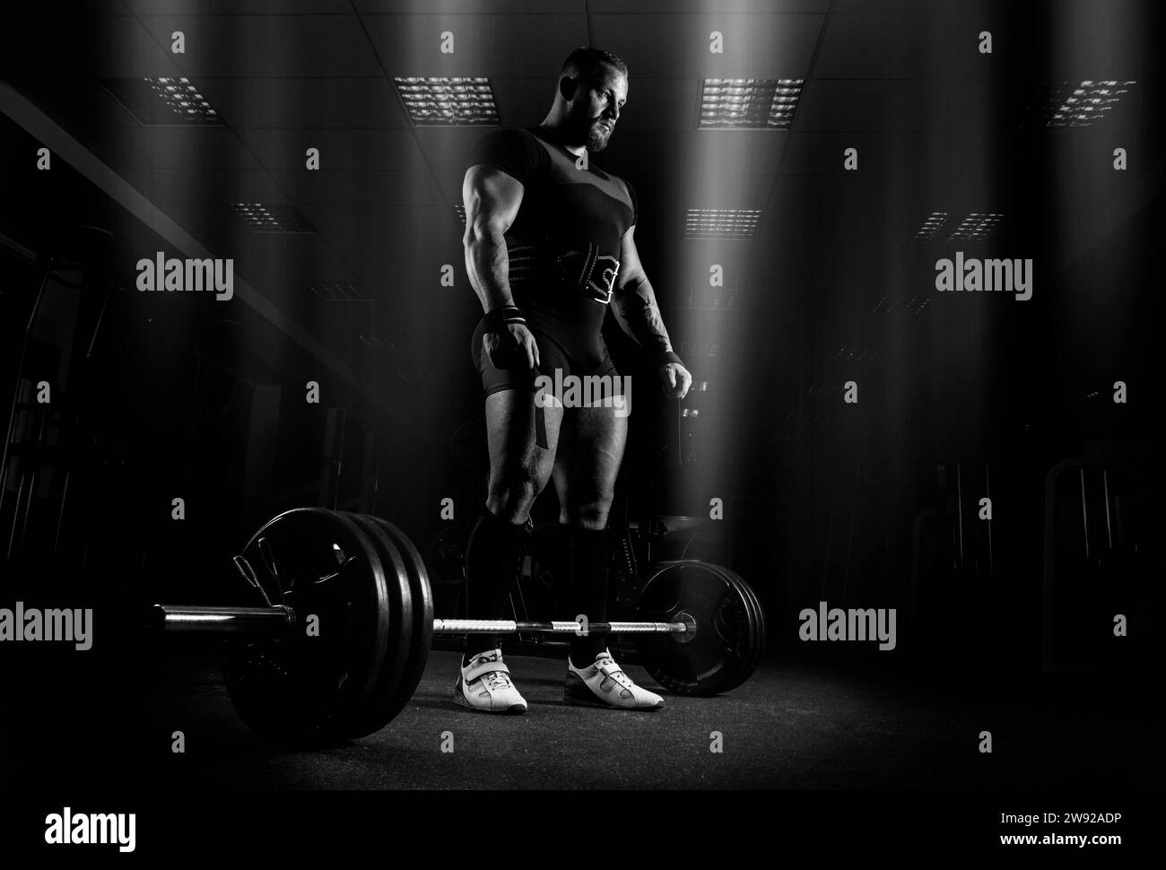 The weightlifter is preparing to perform an exercise called deadlift. He stands directly above the barbell and looks at it Stock Photo