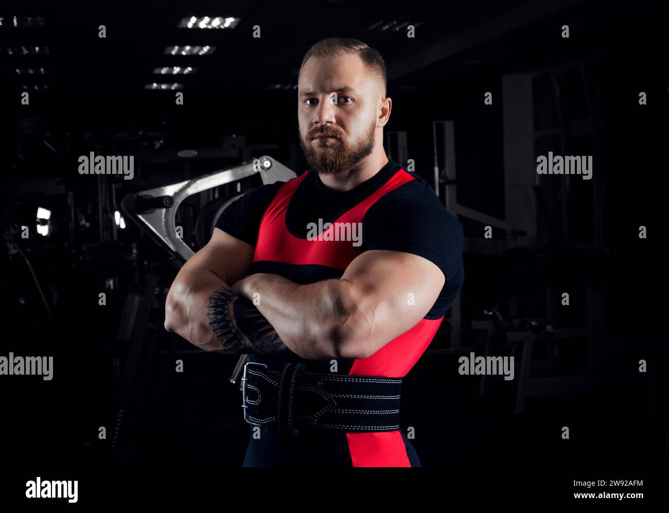The weightlifter stands in a menacing pose with crossed huge arms and looks at the camera Stock Photo