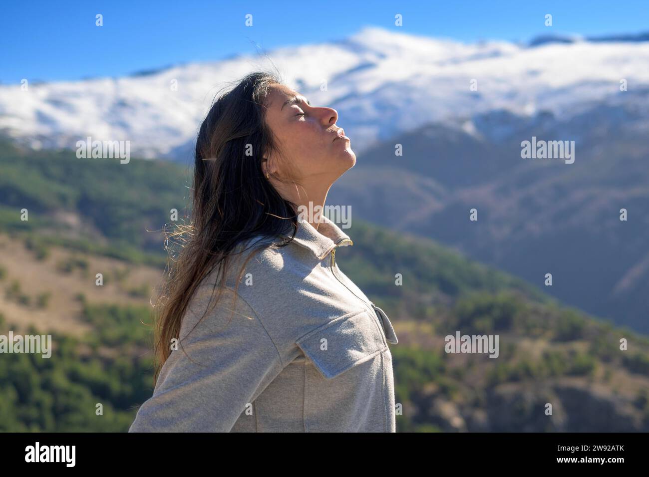 Woman in contemplation facing the sun with snow-capped mountains under a clear sky Stock Photo