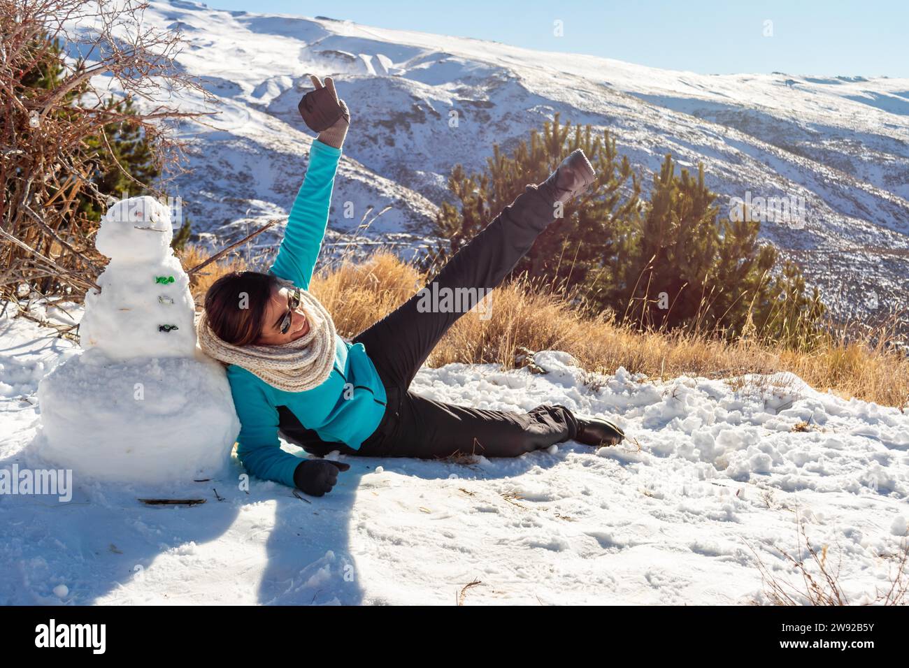Winter Playtime Latina Woman Having Fun Next to Snowman in Snowy Scene Stock Photo