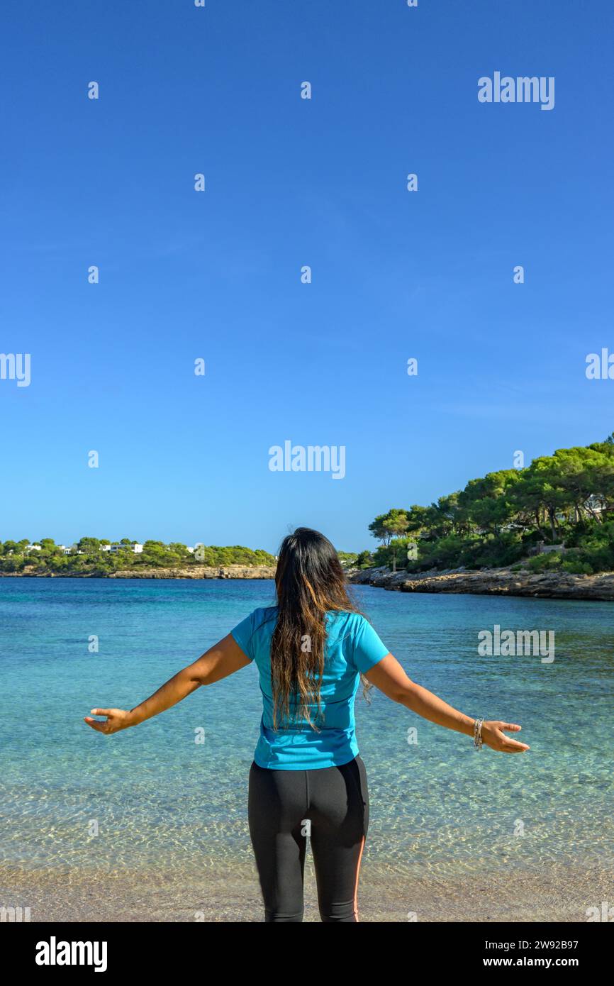 Latina woman, seen from behind, in sportswear, looking at the sea, breathing deeply Stock Photo