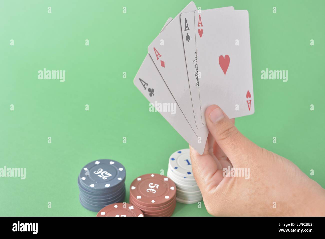 Four aces in a hand with various denomination poker chips on a green felt background, poker