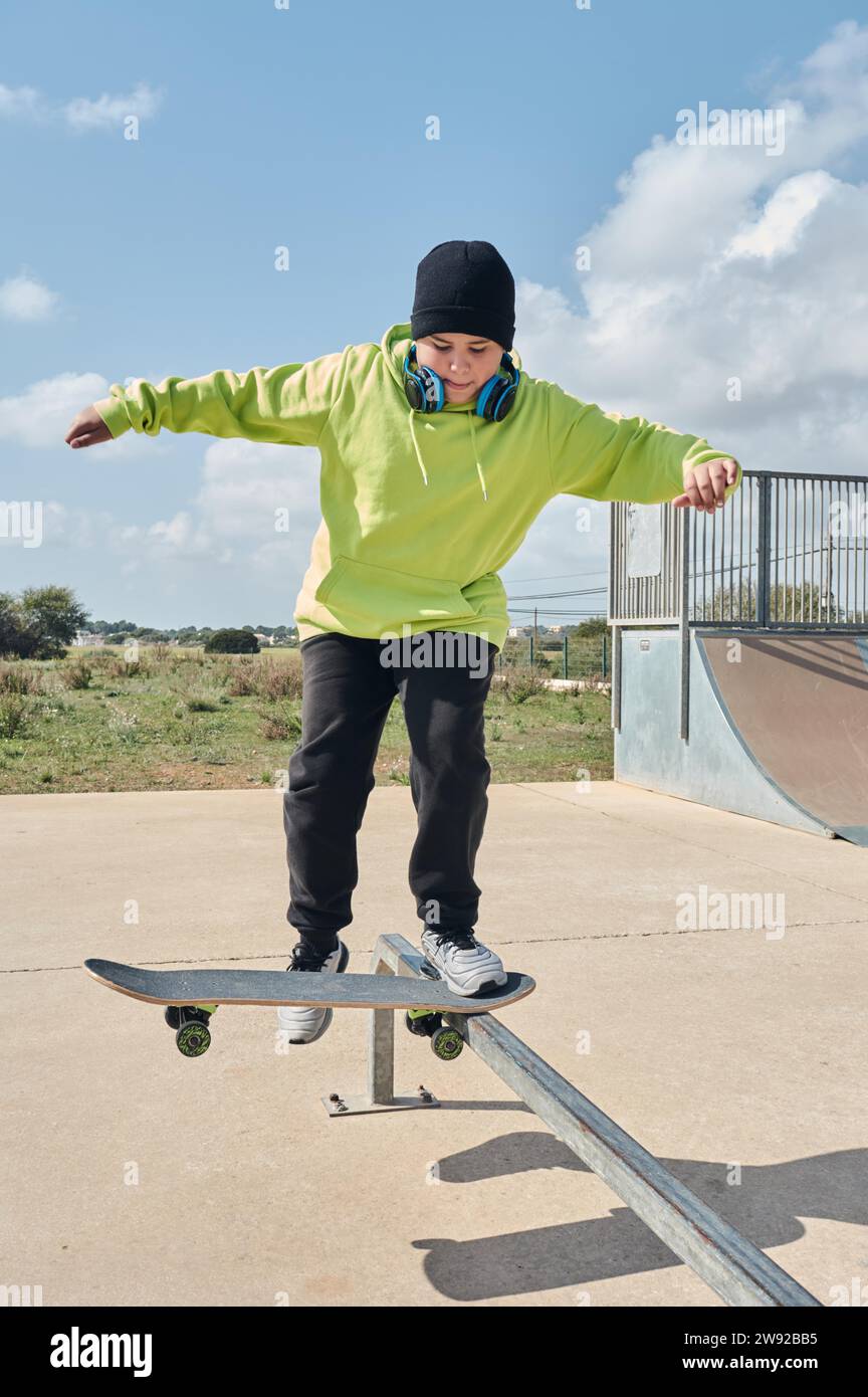 Young, teenager, skateboarding, jumping, on the rink, wearing headphones, green sweatshirt, black hat, swinging Stock Photo