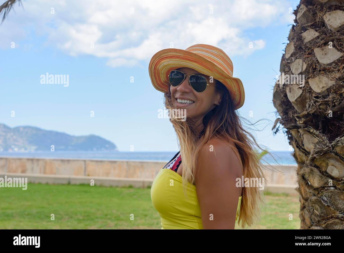 Portrait of a latin woman smiling, having fun, on vacation in mallorca posing on a warm spring summer day, under a palm tree, hollidays Stock Photo