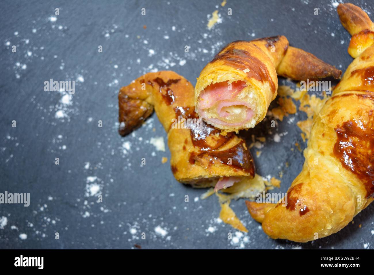 Sliced baked pastry with ham and cheese on a dark background, dusted with a powdery substance, homemade croissant stuffed and cut in half Stock Photo