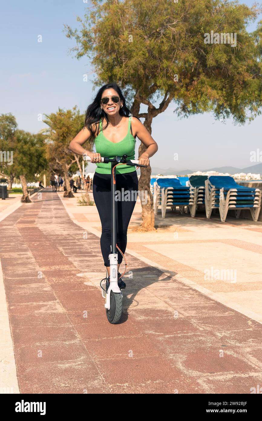 Young latina woman having fun with electric scooter by the beach Stock Photo