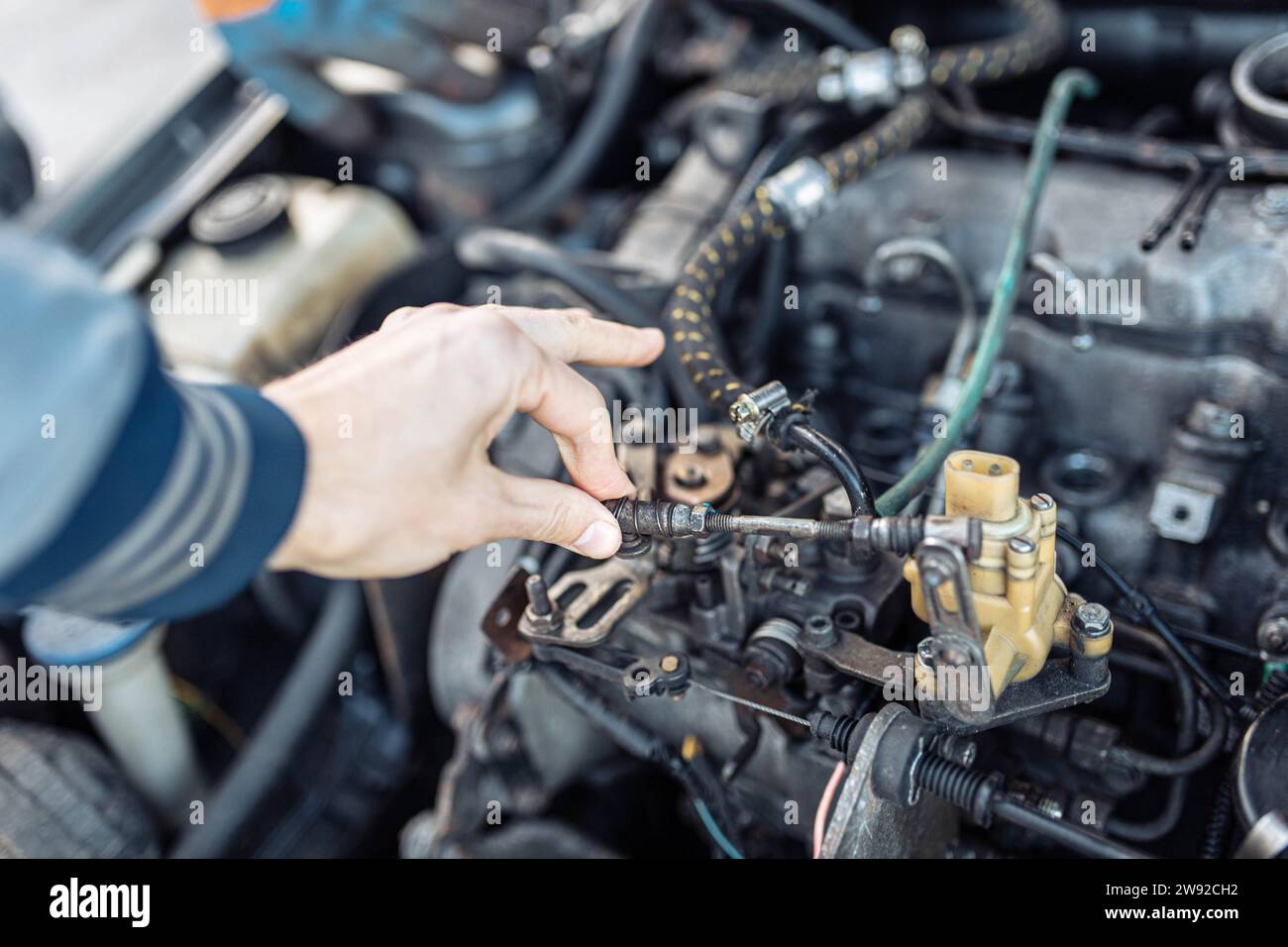 Auto mechanic regulates fuel supply with throttle cable lever, idle setting Stock Photo
