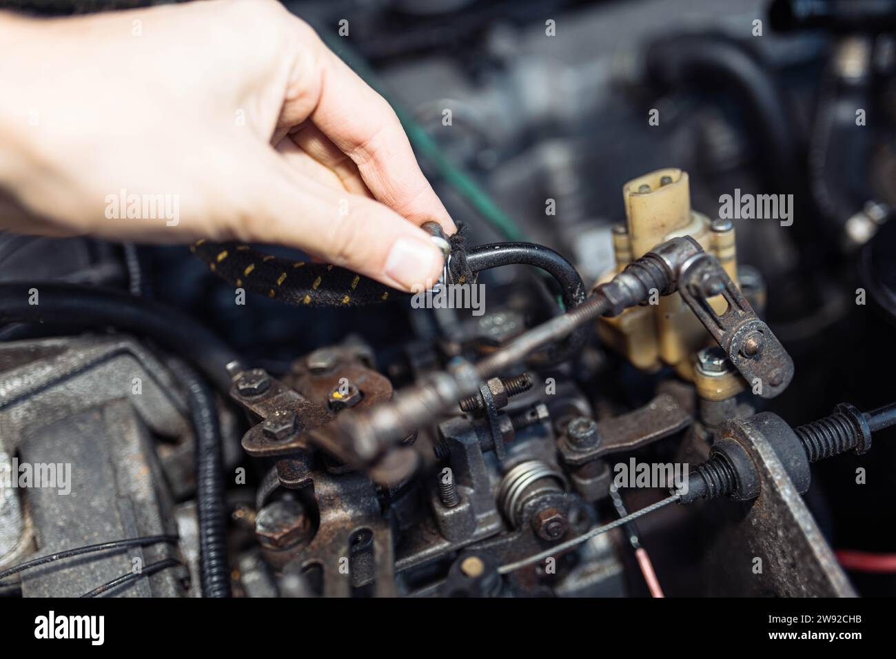 Auto mechanic regulates fuel supply with throttle cable lever, idle setting Stock Photo