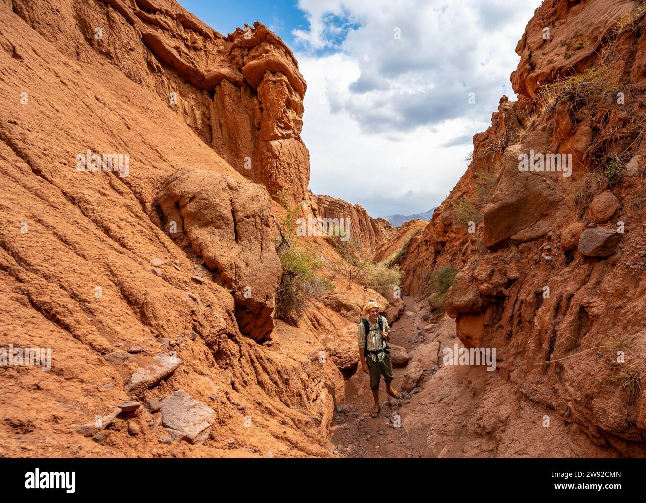 Mountaineer in a canyon with a dry stream bed, eroded mountain landscape with sandstone rocks, canyon with red and orange rock formations, Konorchek Stock Photo