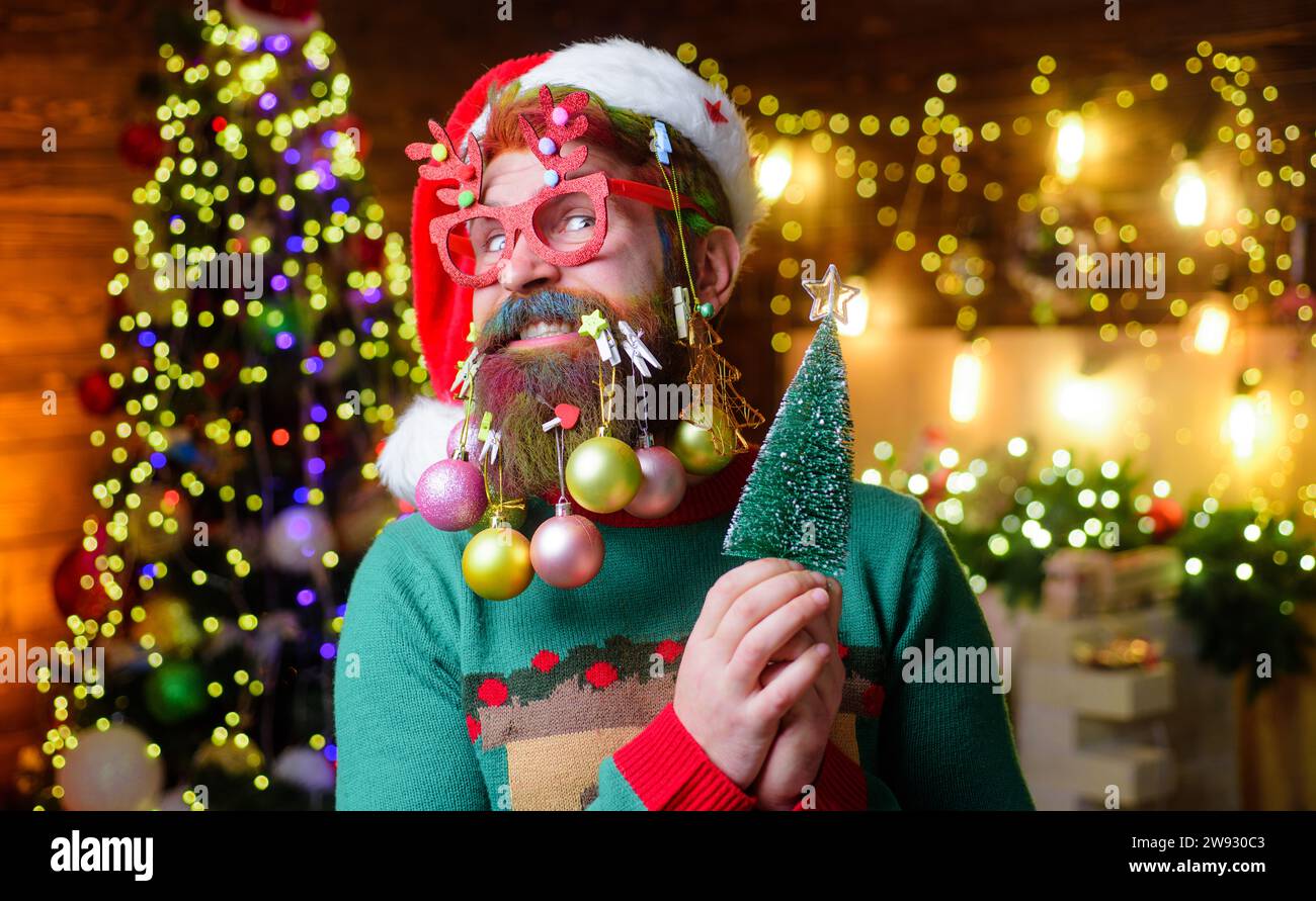 Christmas or New Year barbershop. Winter holidays celebration. Christmas beard style. Funny man in Santa hat with decoration balls in beard. Bearded Stock Photo