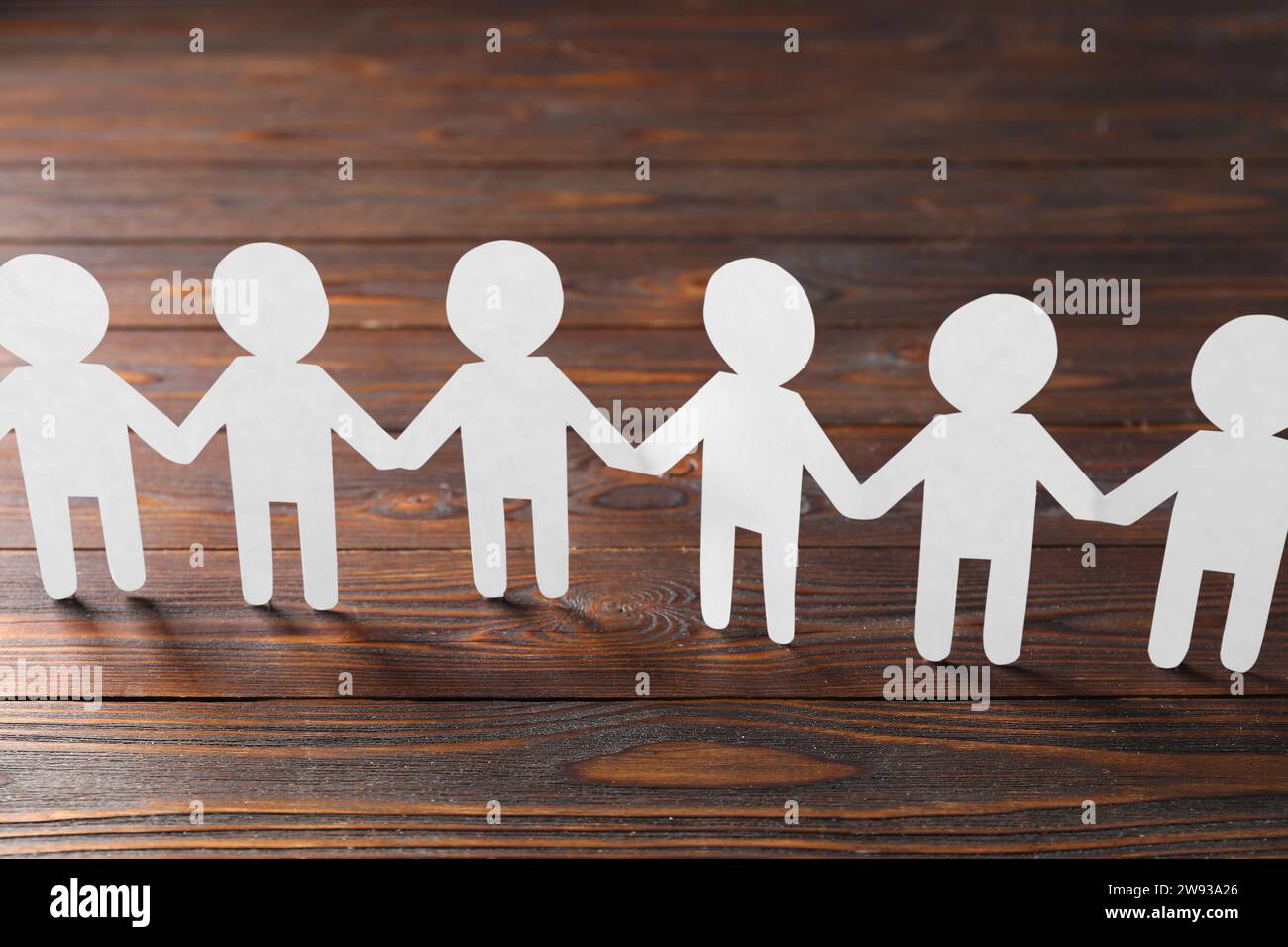 Teamwork concept. Paper figures of people holding hands on wooden table ...