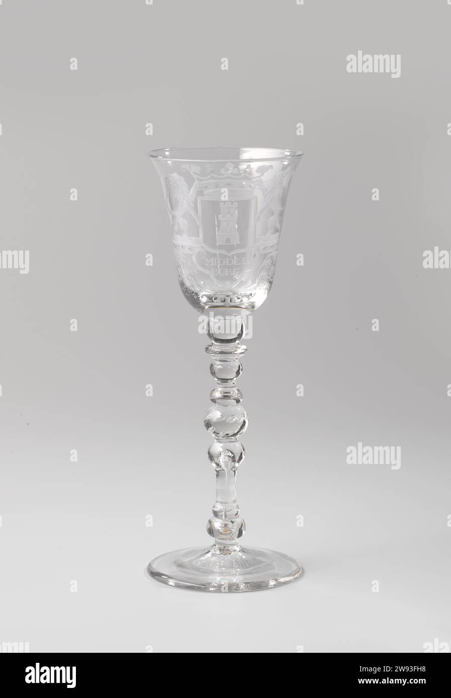 Chalip glass with the weapon of Middelburg, Anonymous, c. 1725 - c. 1750  Chalice glass made of clear, colorless glass. With conical foot. The baluster -shaped trunk with five knots, air bubbles and a double tire of air bubbles. Bell -shaped chalice. On the chalice, on two symmetrical leaves held together by a flower chalice, the crowned weapon of Middelburg flanked by two climbing lions. The name of the city is engraved under the weapon. glassblower: Low CountriesNorthern Netherlands glass   Middelburg Stock Photo