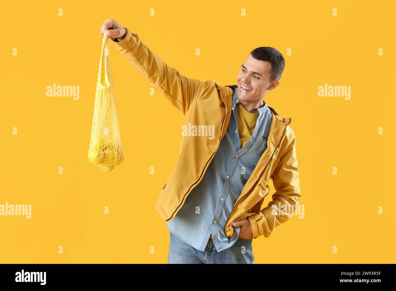 Young man holding string bag with lemons on yellow background Stock Photo