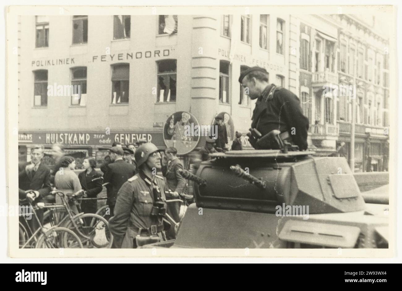 German army in Rotterdam, 1940 photograph German Wehrmacht soldiers, one in a tank with a cap and binoculars, talk to each other on the street in Rotterdam-Zuid. The one on the left has a helmet, wears glasses and binoculars around his neck. The Feyenoord Kliniek can be seen in the background. On the right are Dutch people, with cycling, talking. It would be German tanks of the 9th Armored Division that make contact with the men of the 3rd battalion. The photo was probably taken around the capitulation of the Netherlands on May 15, 1940. Rotterdam photographic support gelatin silver print troo Stock Photo