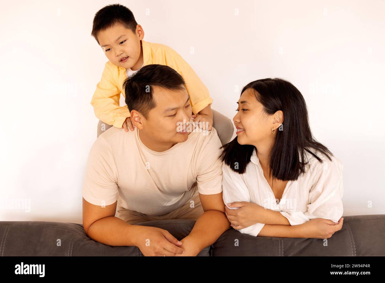 Happy Asian family at home. A Korean couple and their cute little kid on the sofa in the living room. Parents and their son pose together. Stock Photo