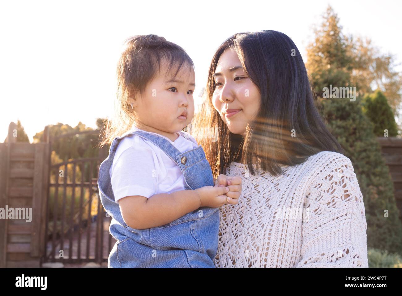 A young Asian woman hugs her little daughter. An attractive mom walks with her cute girl outdoors. Happy Korean family in the park. Stock Photo