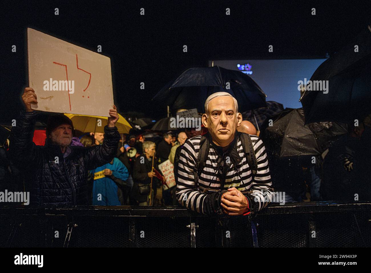 Israel. 23rd Dec, 2023. A protestor in a convict uniform wears a Benjamin Netanyahu mask next to a sign that reads “Go away!” during a demonstration attended by thousands under pouring rain calling Prime Minister Benjamin Netanyahu to resign. Tel Aviv, Israel. Dec 23th 2023. (Matan Golan/Sipa USA). Credit: Sipa USA/Alamy Live News Stock Photo