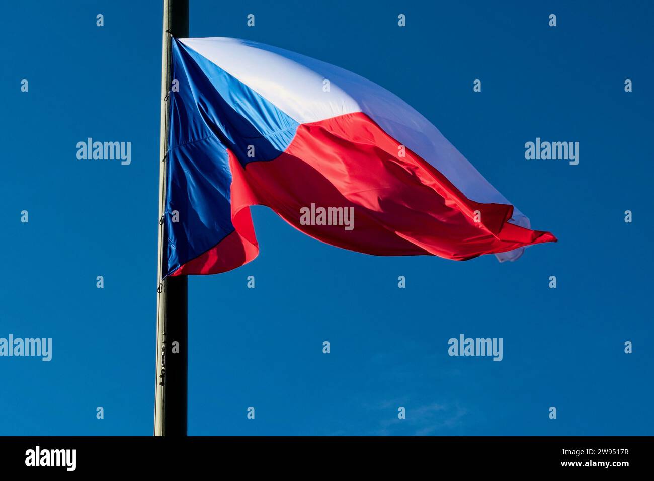 The Czech Republic flag is flying on a flagpole with a blue sky in the background. Stock Photo