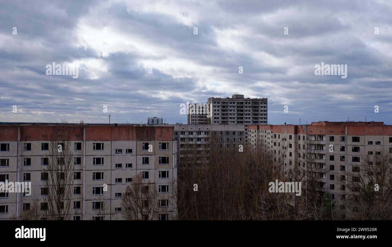 The image shows aged apartments with a backdrop of a dramatic cloudy sky and leafless trees. Stock Photo
