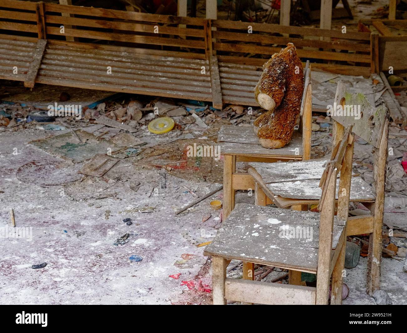 The image shows a neglected room with a teddy bear on a chair. Dirty plush toy on the chair. A headless teddy bear in an abandoned kindergarten in Pri Stock Photo