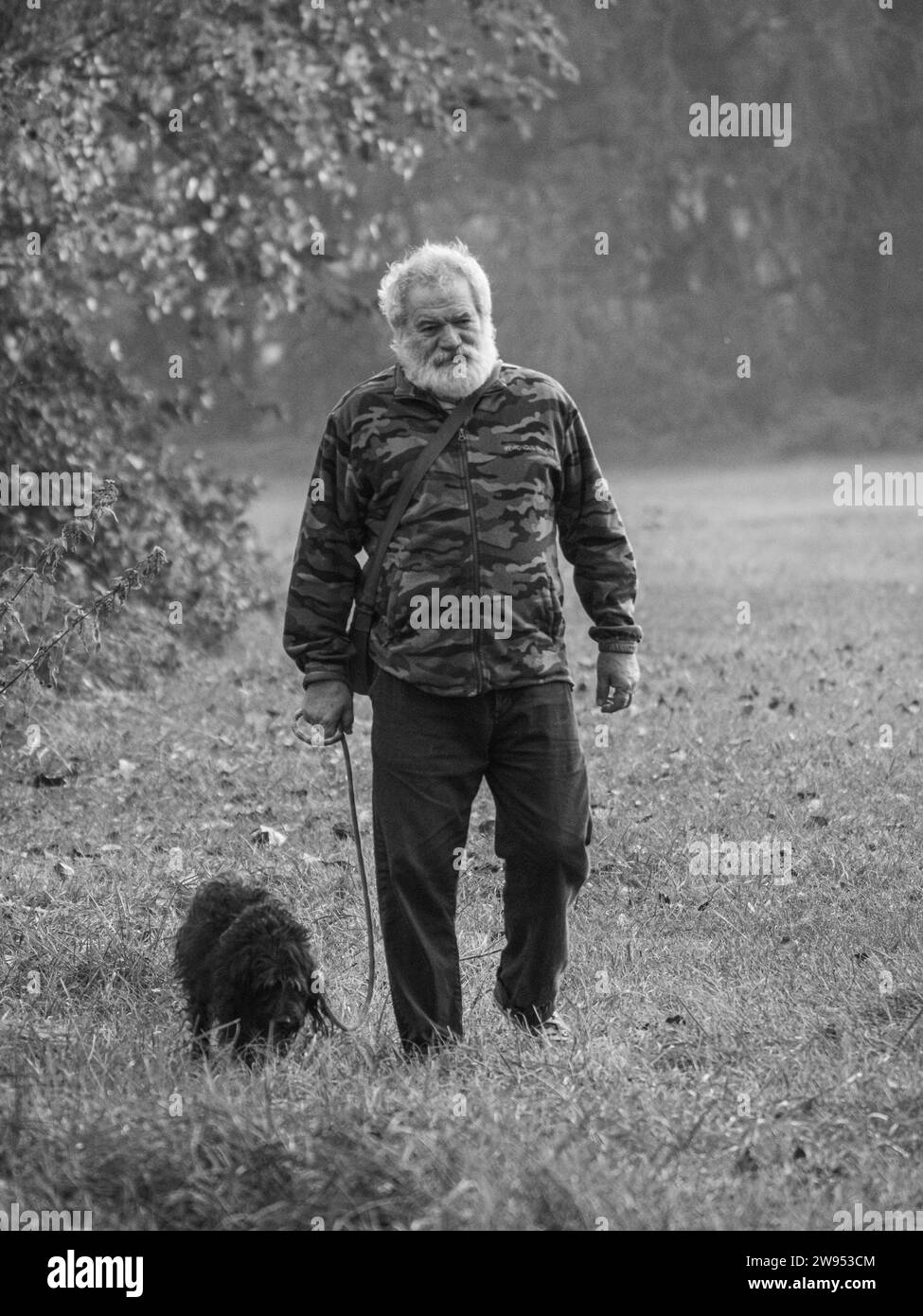 senior caucasian man walking a black terrier dog outdoors in a park in autumn seaon Stock Photo