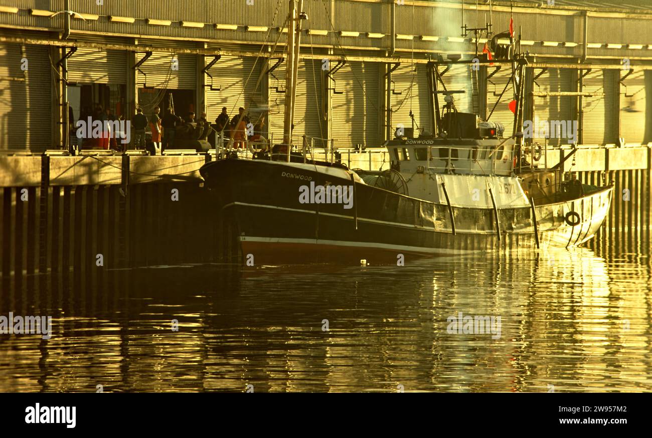 Aberdeen Harbour and fish market a group of fishermen and a fishing vessel in the early morning sunshine Stock Photo