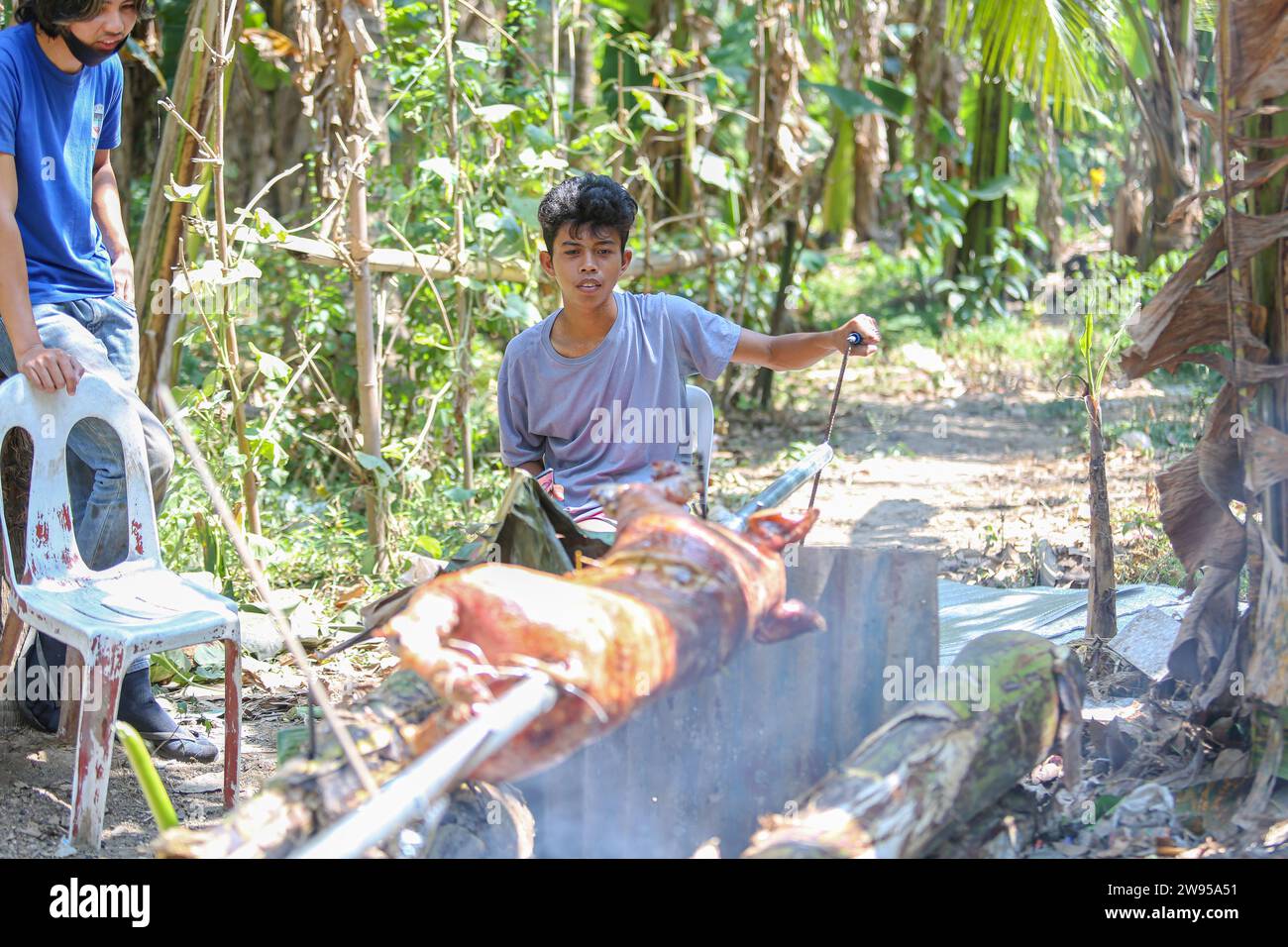 Calamba, Philippines. December 24, 2023 : Filipinos preparing suckling pig in rural style, onions/lemongrass stuffed, roasted over charcoal framed by banana tree trunks in forest. Known as lechon, it's a staple of holidays celebrations in the Christmas-obsessed Philippines. Leftovers will be made into a vinegar stew. Farmer say: 'Lechon has always been a luxury out of reach for many Pinoys (from $100 to $250). Before, we bought it from suppliers. With inflation, we can't afford. We resumed our practice of preparing/cooking it ourselves, old-fashioned way'. Credit: Kevin Izorce/Alamy Live News Stock Photo