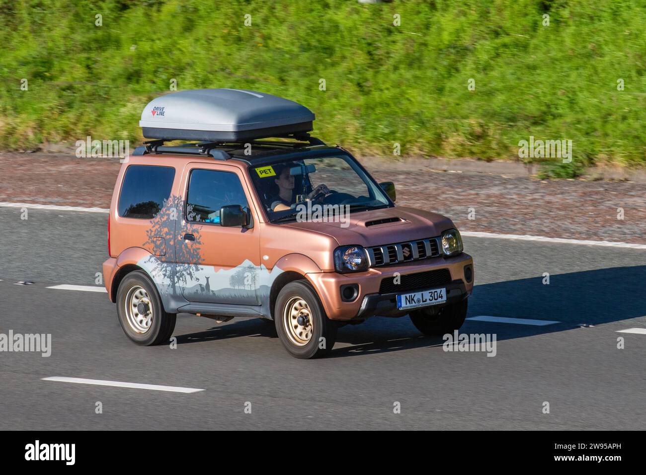 2017 bespoke German Suzuki Jimny  European country of origin number plate.  LHD SUV with roof rails and DriveLine roof box decorated with mountain decals, stickers and tree forest graphics. Suzuki Jimny SZ4 Auto Sport utility vehicle driving on the M6 motorway near Preston in Lancashire, UK Stock Photo