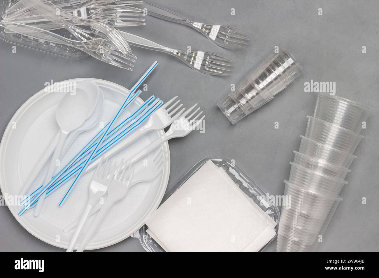 Disposable white plastic tableware. Plate, spoons, forks, straws for drinks. Plastic processing problem. Ecology environmental care. Flat lay. Grey ba Stock Photo