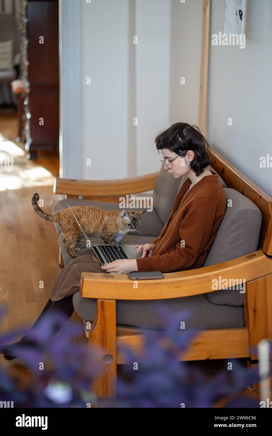Teenager working at home, studying online, and fluffy companion diverting girl attention from work Stock Photo
