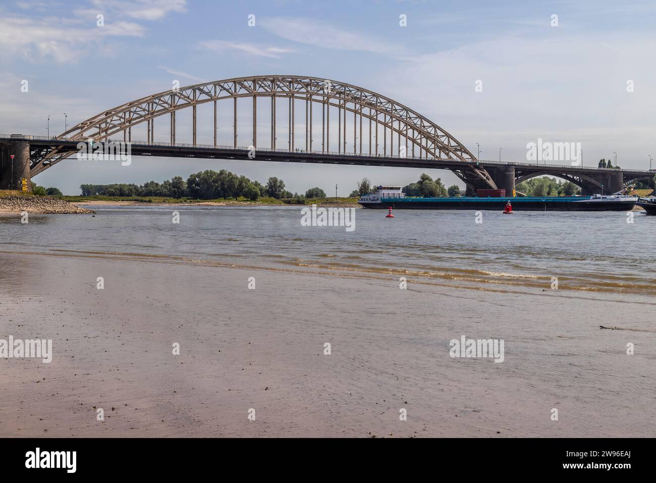 Cargo ship sails at very low tide under the Waal Bridge - Waalbrug, near the Dutch city of Nijmegen. Stock Photo